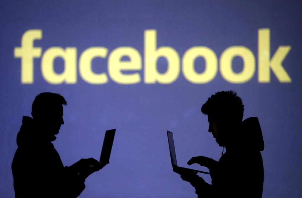 Silhouettes of laptop users are seen next to a screen projection of Facebook logo in this picture illustration taken on March 28, 2018. — Reuters
