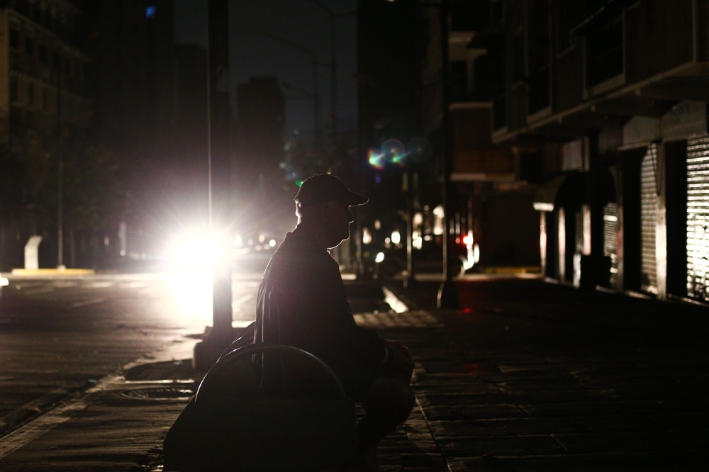 A man sits on a bench in pitch dark,  during a power cut in Caracas, Venezuela, on Wednesday. — AFP