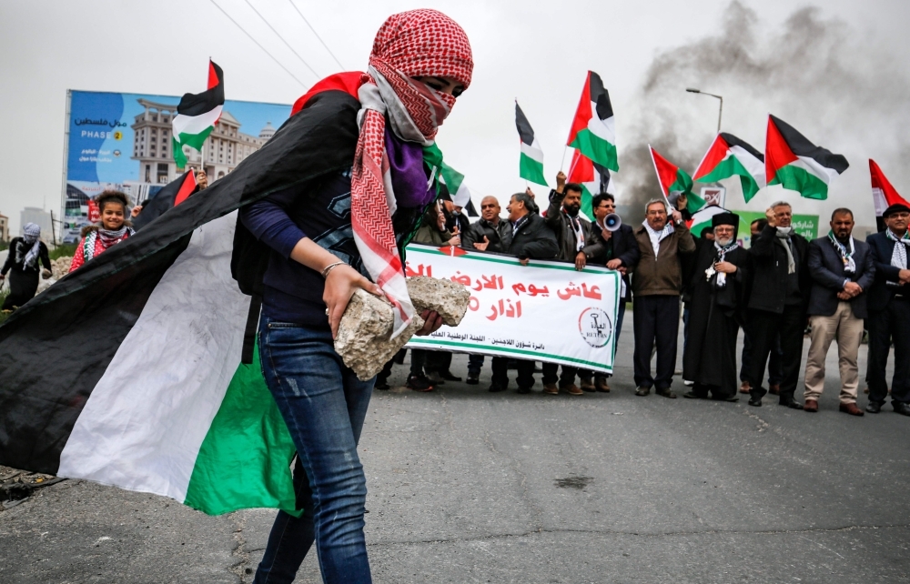 A Palestinian girl with her face covered with traditional chequered keffiyeh carries a stone during clashes with Israeli forces following a demonstration marking 