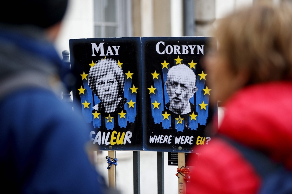 Pedestrians walk past placards featuring Britain’s Prime Minister Theresa May and opposition Labour party leader Jeremy Corbyn near the Houses of Parliament in central London on Wednesday. — AFP