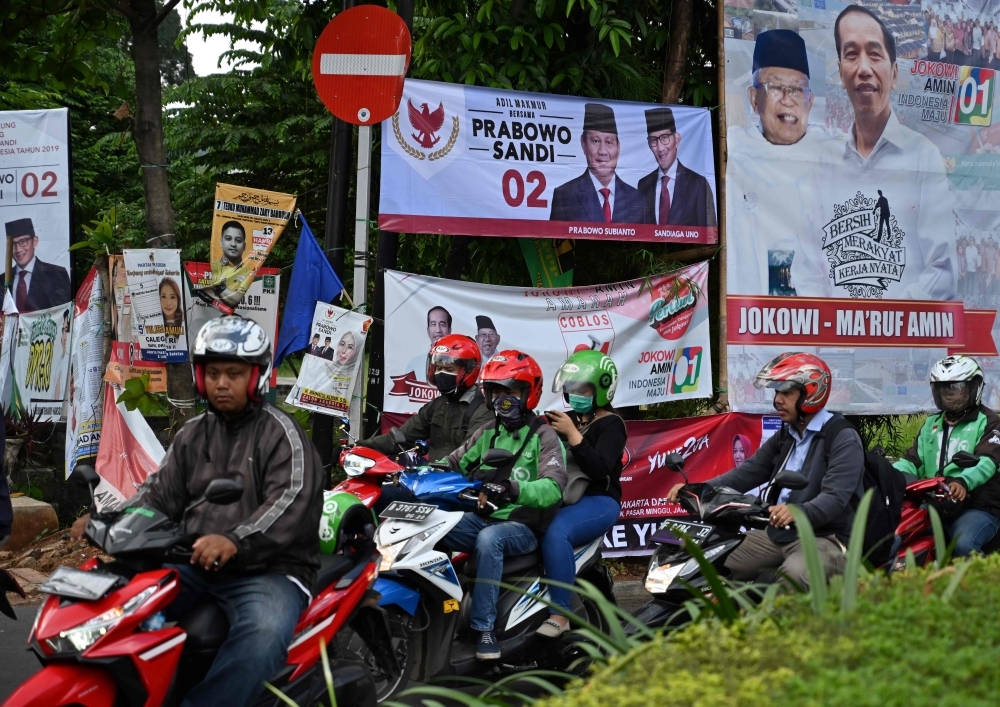 Commuters during rush hour passing banners for various presidential and vice presidential candidates in Jakarta. — AFP