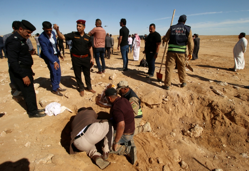 Iraqi members of the Civil Defense and Kurdish men examine an unearthed mass grave of Kurds in west of the city of Samawa, Iraq, Sunday. — Reuters