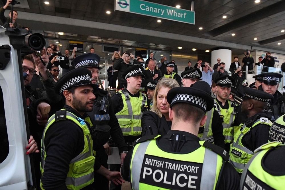Police escort away an arrested female climate change protester, center, who had glued herself to the roof of a DLR train at Canary Wharf station, on the third day of an environmental protest by the Extinction Rebellion group, in London on Wednesday. — AFP