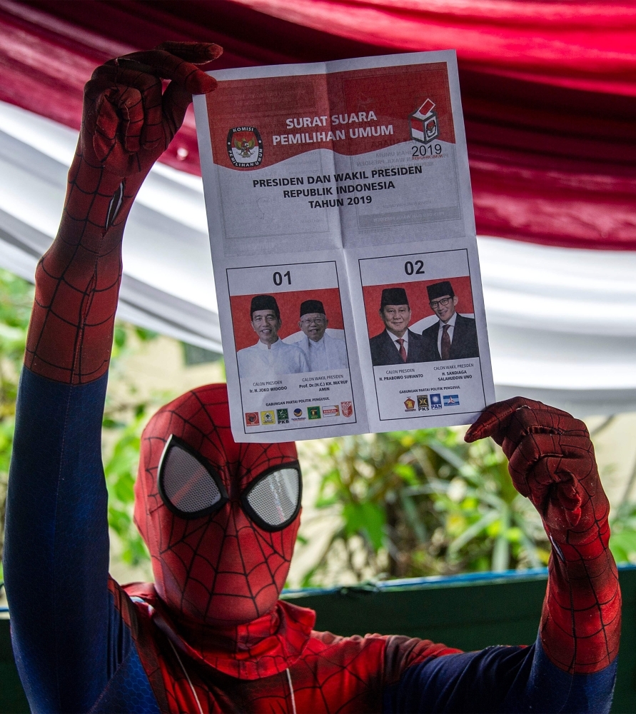 An Indonesian election worker dressed in a superhero costume holds up a ballot paper at a polling station in Surabaya on Wednesday. — AFP