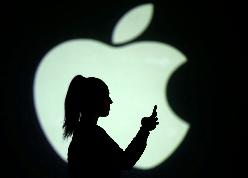 Silhouette of mobile user is seen next to a screen projection of Apple logo in this picture illustration. — Reuters