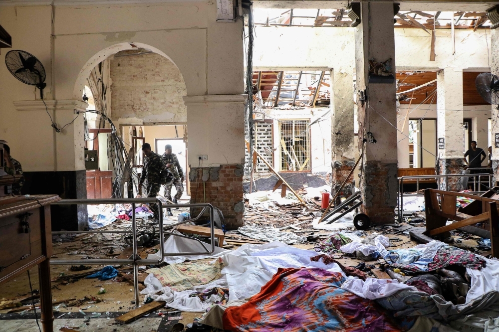 Sri Lankan security personnel walk next to dead bodies on the floor amid blast debris at St. Anthony's Shrine following an explosion in the church in Kochchikade in Colombo on Sunday. — AFP