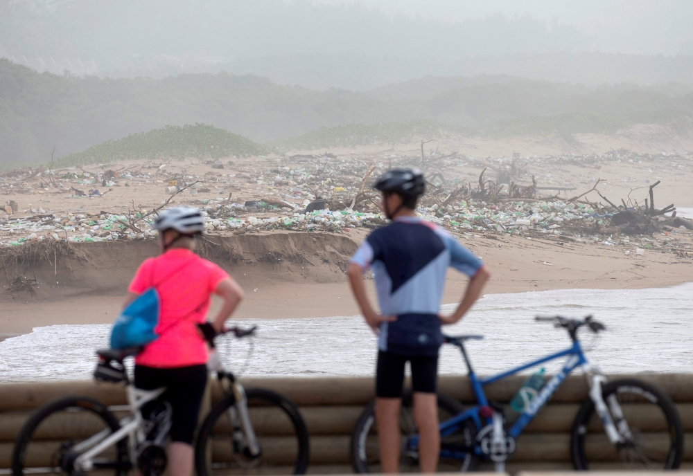 Cyclists look at debris on the beach after massive flooding in Durban, South Africa, on Wednesday. — Reuters