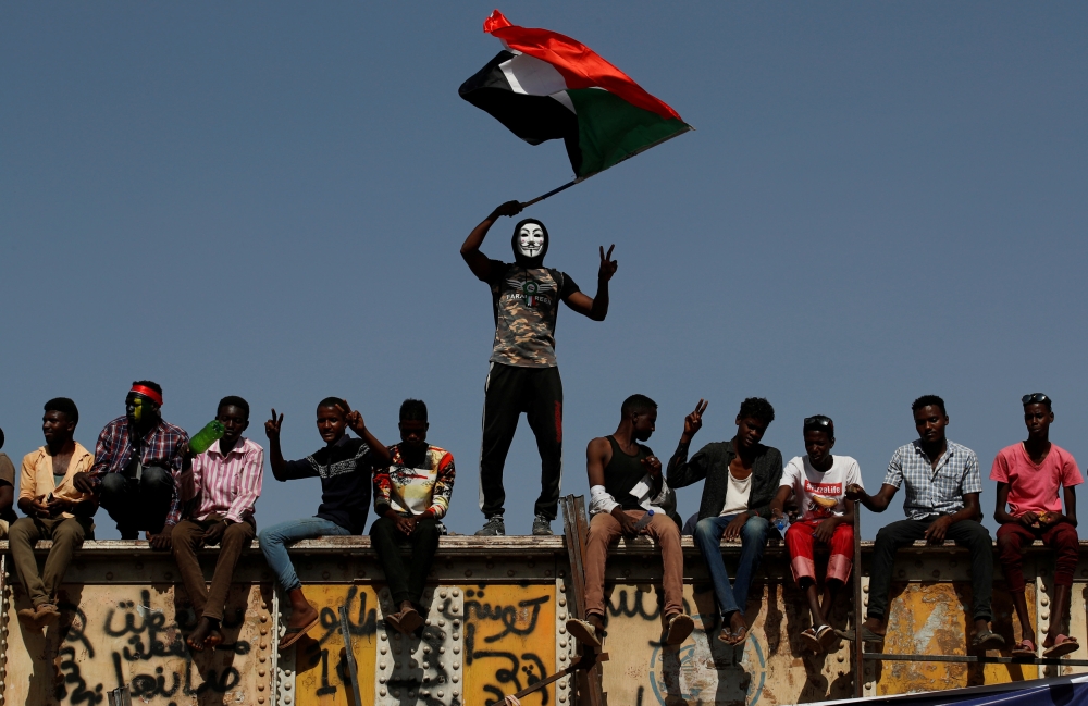 A Sudanese protester wearing a Guy Fawkes mask waves a national flag outside the defense ministry compound in Khartoum, Sudan, on Wednesday. — Reuters