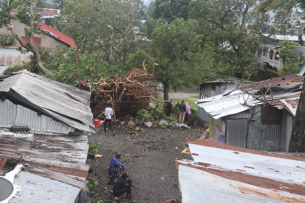 People stand by damaged houses and fallen trees on Thursday in Moroni after tropical storm Kenneth hit Comoros before heading to recently cyclone-ravaged Mozambique. — AFP