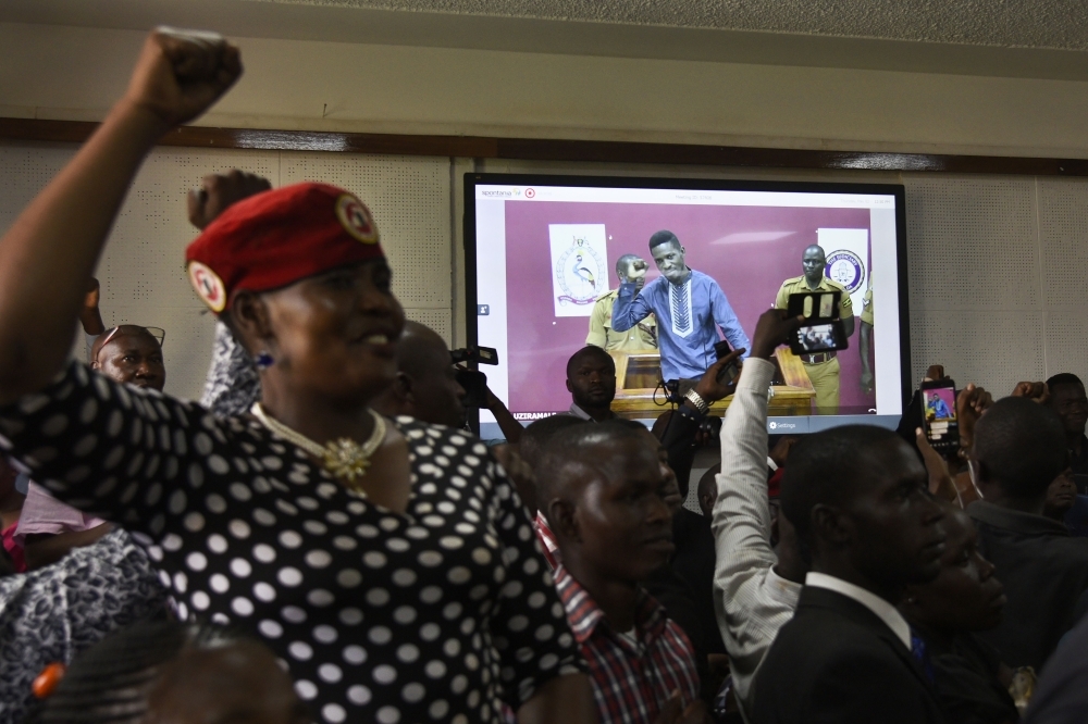 Supporters of Ugandan musician turned politician, Robert Kyagulanyi a.k.a. Bobi Wine react as he gestures attending a court via video link in Kampala on Thursday. — AFP