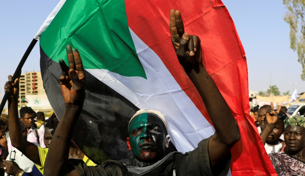 A Sudanese protester gestures as another waves a national flag during a demonstration in front of  the defense ministry compound in Khartoum on Friday. — Reuters