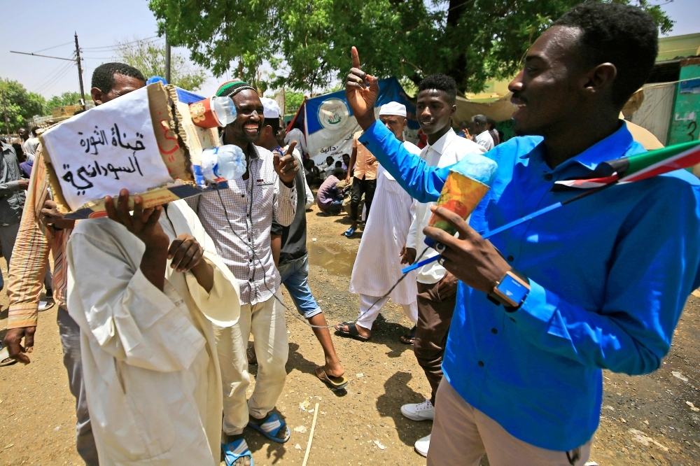 A Sudanese protester carrying a mock-camera interviews a fellow protester outside Sudan's army headquarters in Khartoum.  -AFP 