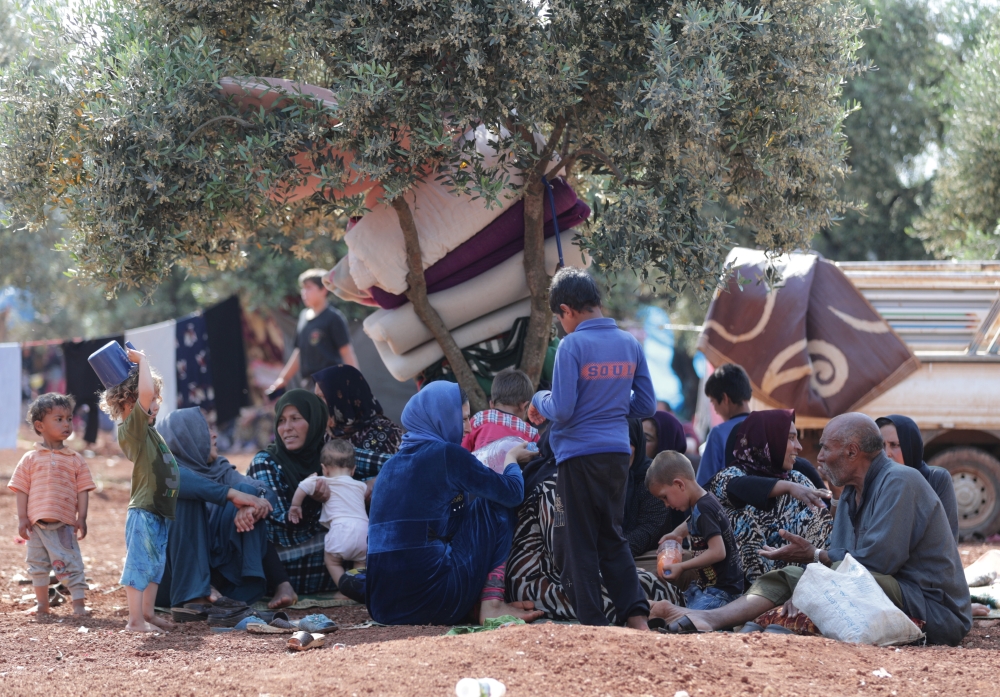 Displaced Syrians sit together in an olive grove in Atmeh town, Idlib province, Syria, on Wednesday. — Reuters