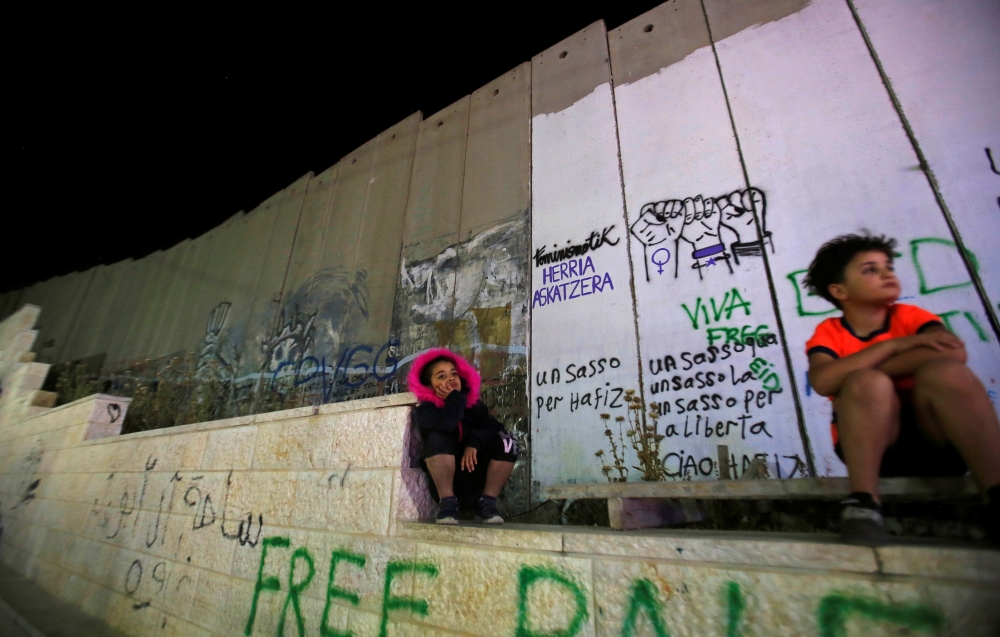 Palestinian children sit near the Israeli barrier as they watch Globalvision event to protest against the Eurovision Song Contest hosted by Israel, in Bethlehem in the Israeli-occupied West Bank, on Saturday. — Reuters