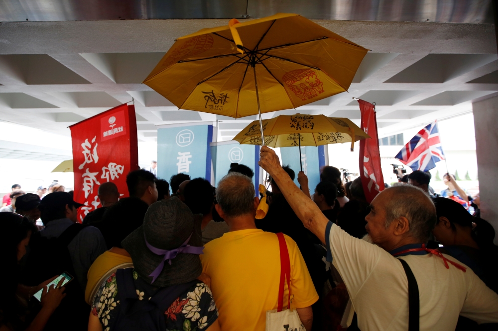 Activists hold umbrellas as Hong Kong's pro-democracy activist Joshua Wong speaks to members of the media at the High Court in Hong Kong, May 16. - Reuters