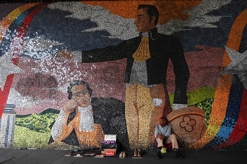 A street vendor sits in front of a mural depicting Venezuelan national hero Simon Bolivar, in Caracas on May 21. - AFP  
