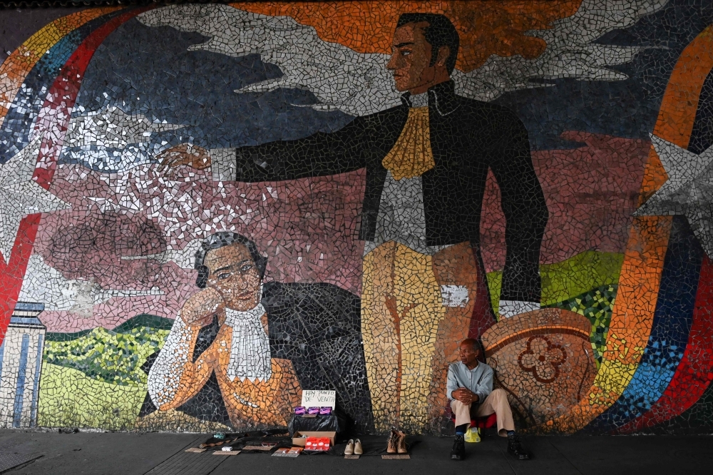 A street vendor sits in front of a mural depicting Venezuelan national hero Simon Bolivar, in Caracas on May 21. - AFP  