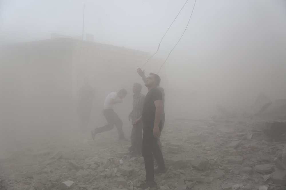A Syrian man gestures as others run for cover during air strikes by pro-regime forces on the market town of Kfar Ruma in Syria's southwestern Idlib province on Thursday. — AFP
