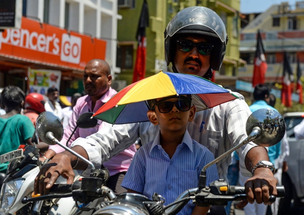 An Indian boy wears an umbrella hat as he is carried by a man riding a bike on a hot day in Chennai on Wednesday. — AFP