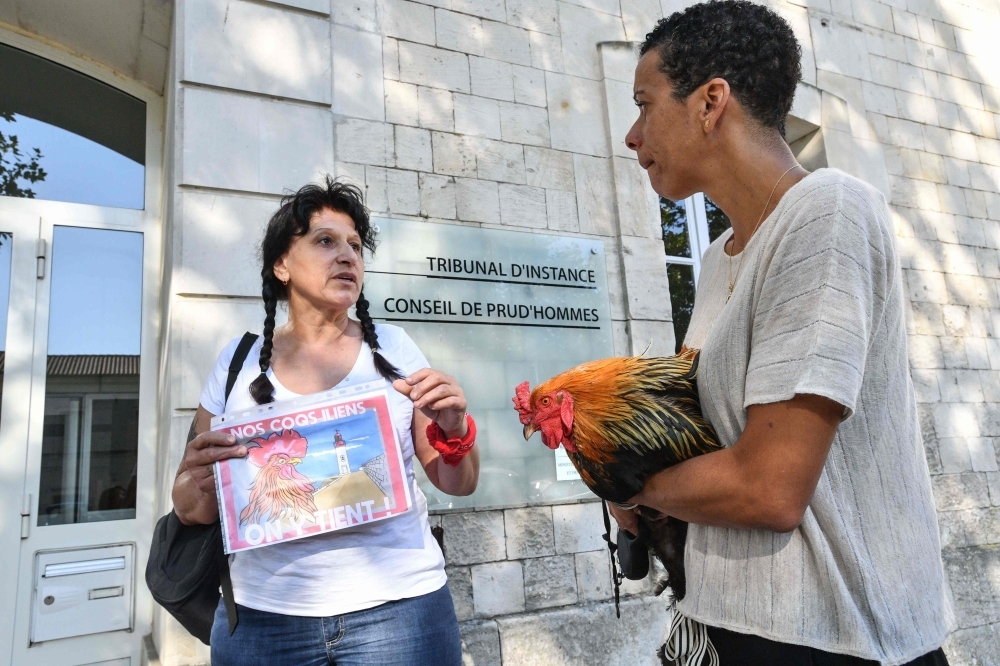 A woman holds a rooster in her arms and talks to a supporter holding a banner reading 