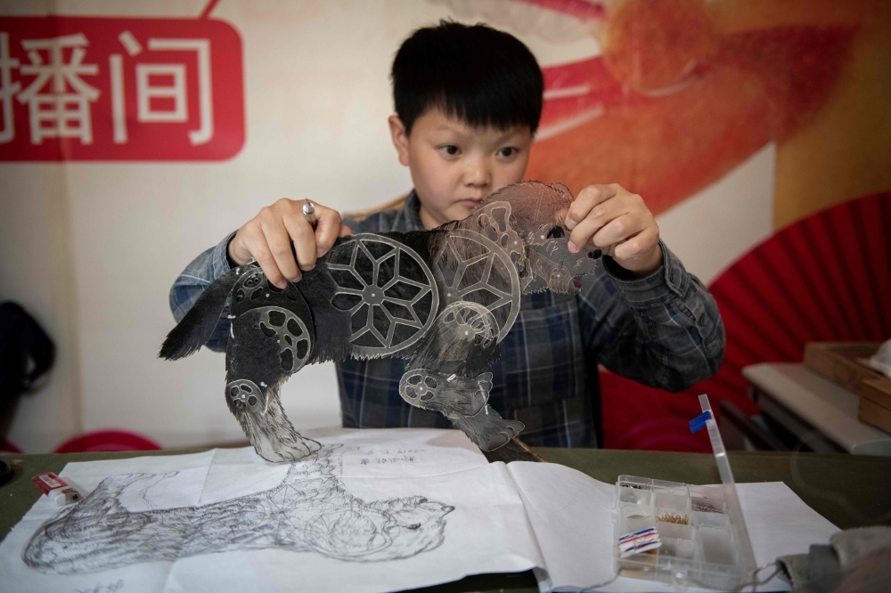 In this picture taken on May 9, 2019, Jin Xinchun, a member of the Flying Dragon Troupe, creates a shadow puppet at the troupe's studio on the outskirts of Beijing. Shadow puppets flitting across screens and reliving age old stories have fascinated Chinese people for some 2,000 years, but falling audiences mean troupes are having to be creative to stay on the stage. — AFP