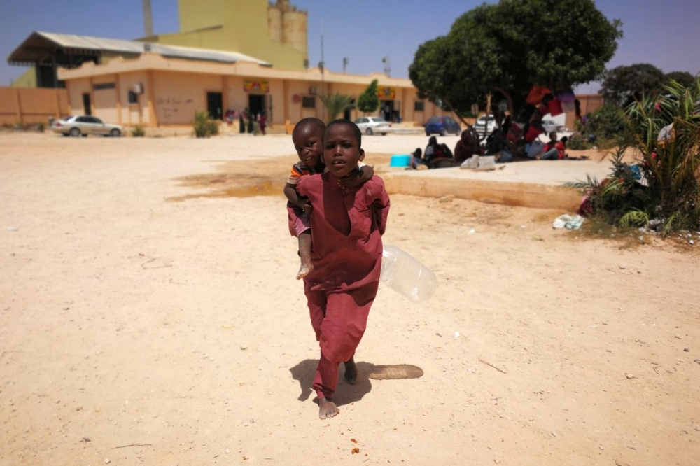 A migrant carries a child on her back in Ganfouda detention centre in west of Benghazi, Libya, on Wednesday. — Reuters