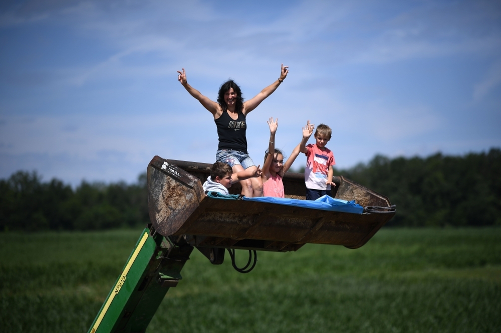 Cycle race enthusiasts gesture as they sit in the bucket of a backhoe loader parked on the roadside during the seventh stage of the 106th edition of the Tour de France cycling race between Belfort and Chalon-sur-Saone, on Friday. — AFP