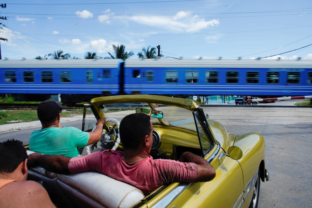 People wait in a vintage car as Cuba's Chinese-made new train passenger cars move after departing from La Coubre train station in Havana on Saturday. -Reuters