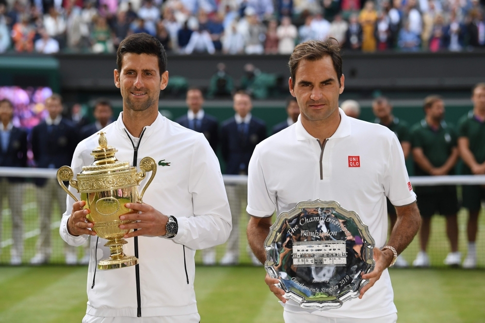 Serbia's Novak Djokovic (L) poses with the winner's trophy and Switzerland's Roger Federer (R) holds the runners up plate during the presentation after the men's singles final on day thirteen of the 2019 Wimbledon Championships at the All England Lawn Tennis Club in Wimbledon, southwest London, on Sunday. — AFP
