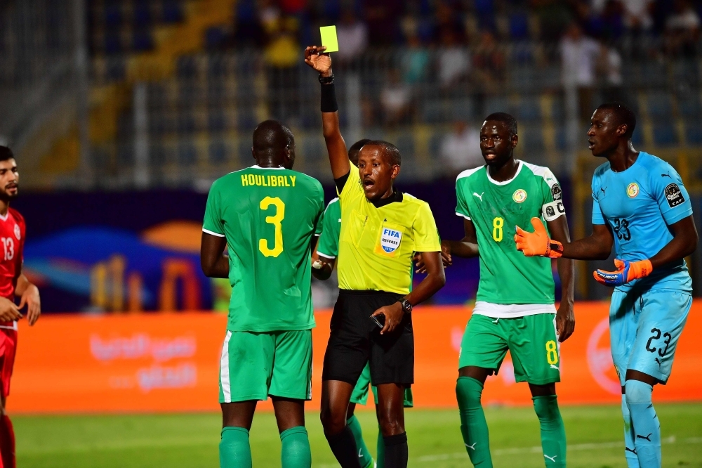 Ethiopian referee Bamlak Tessema Weyesa (C) shows a yellow card to Senegal's defender Kalidou Koulibaly (L) during the 2019 Africa Cup of Nations (CAN) semifinal football match between Senegal and Tunisia at the 30 June stadium in Cairo, on Sunday. — AFP