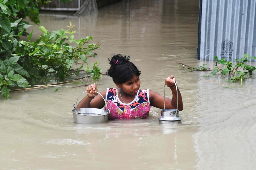 An Indian girl carries drinking water as she wades through flood waters at Pabhokathi village in Morigaon district of India's Assam state on Monday. — AFP