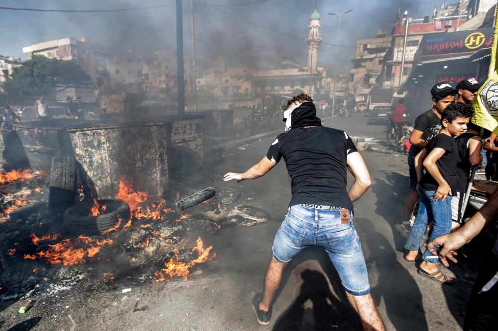 A masked man throws a tire into a fire as protesters block the main road outside the Palestinian refugee camp of Burj Al-Barajneh, south of the Lebanese capital Beirut, on Tuesday, during a protest against a decision by the Lebanese government to impose restrictions on the Palestinians' work opportunities. — AFP