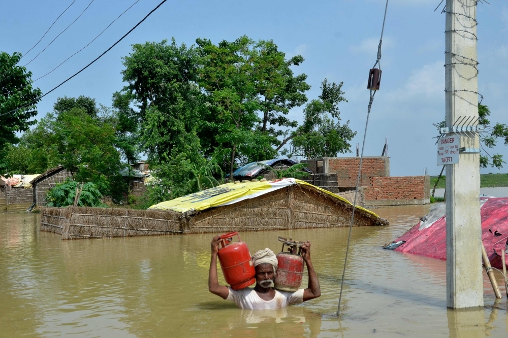 An Indian resident carries gas canisters as he wades through a flooded area following heavy monsoon rains in Muzaffarpur in the Indian state of Bihar on Tuesday. — AFP