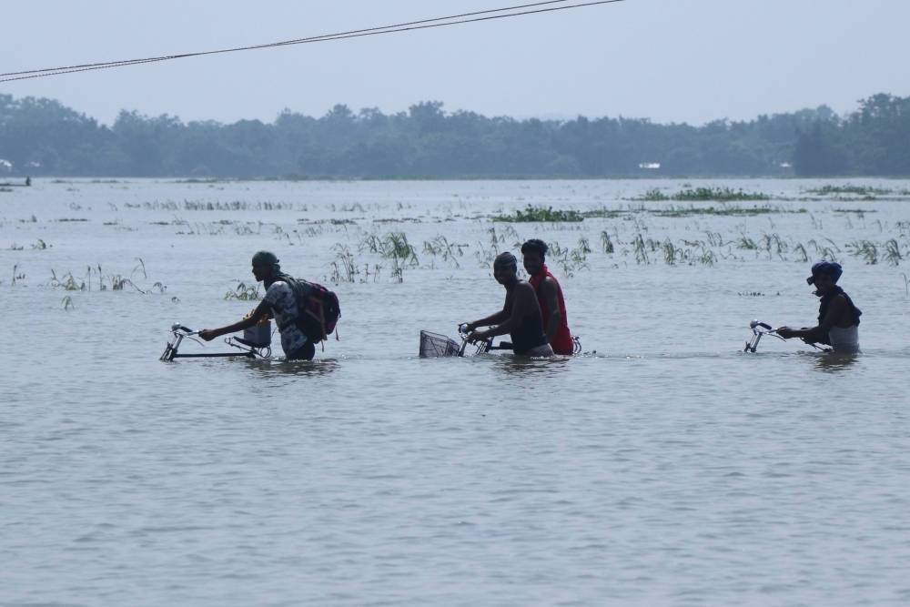 Villagers cross a submerged road with their bicycles in the flood affected area of Boko, in Kamrup district of Assam, India, on Thursday. — AFP