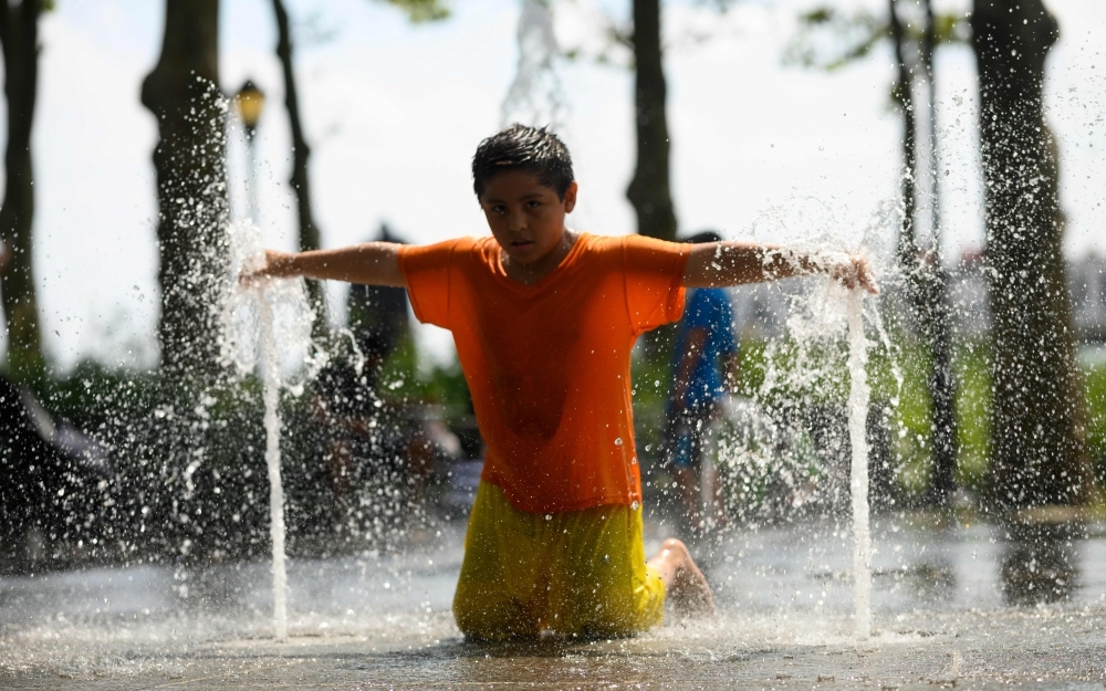 Children cool down as they play in a public fountain during summer heat on Friday in New York City. -AFP photo