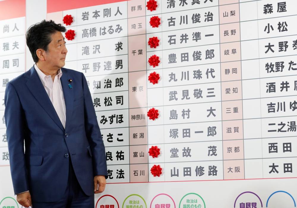 Japan's Prime Minister Shinzo Abe, who is also leader of the ruling Liberal Democratic Party (LDP), looks at a chart with rosettes put on the names of candidates who are expected to win the upper house election, at the LDP headquarters in Tokyo, Japan, on Sunday. — AFP