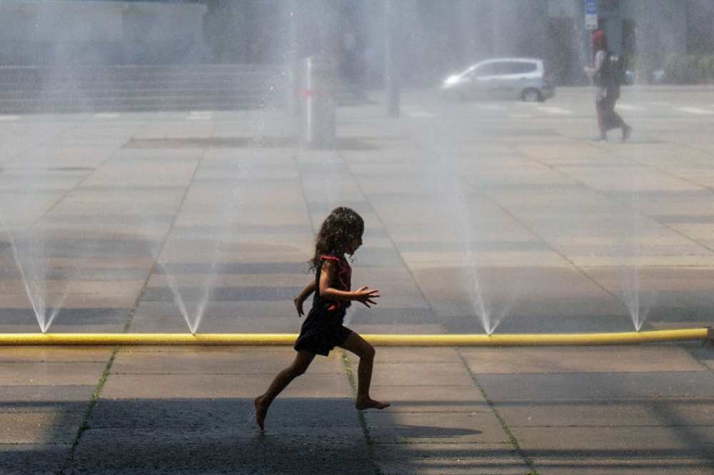 A girl runs through water sprayed from a pipe at Praterstern Square in Vienna on Thursday. — AFP