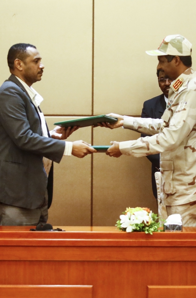 Gen. Mohamed Hamdan Daglo (right), Sudan's deputy head of the Transitional Military Council, and protest leader Ahmed Rabie exchange the constitutional declaration after signing it at a ceremony attended by African Union and Ethiopian mediators in Khartoum, Sunday. — AFP