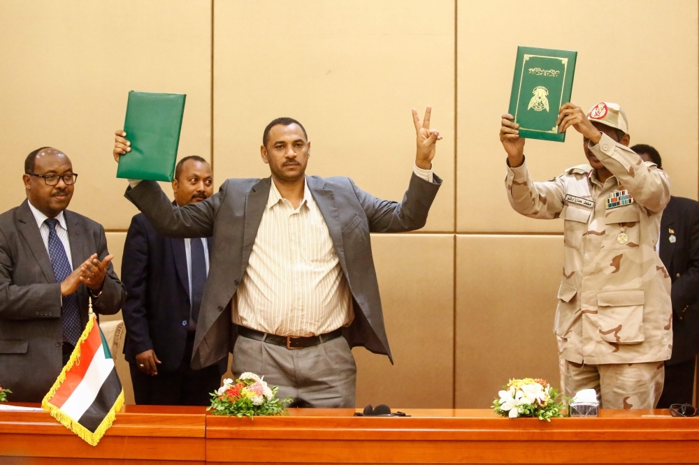 Gen. Mohamed Hamdan Daglo (right), Sudan's deputy head of the Transitional Military Council, and protest leader Ahmed Rabie exchange the constitutional declaration after signing it at a ceremony attended by African Union and Ethiopian mediators in Khartoum, Sunday. — AFP