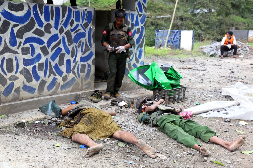   A Myanmar army soldier stands near the bodies of his fellow soldiers who were killed in an insurgent attack on the Myanmar-China major trading route in Nawnghkio township, Shan state, Myanmar on Thursday. -Reuters