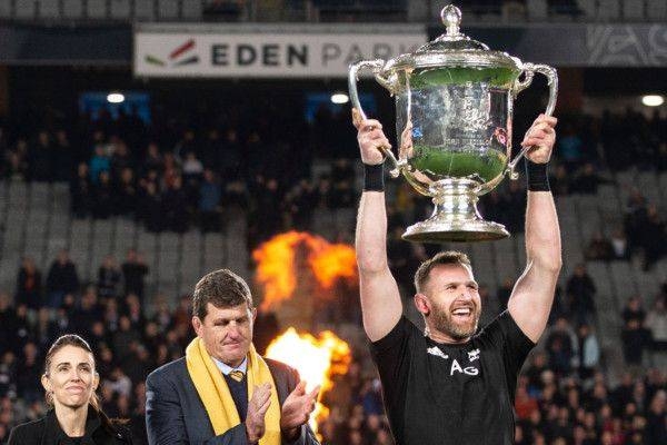 New Zealand captain Kieran Read holds aloft the Bledisloe Cup as New Zealand Prime Minister Jacinda Ardern (left) savors the moment of triumph in Auckland. — AFP