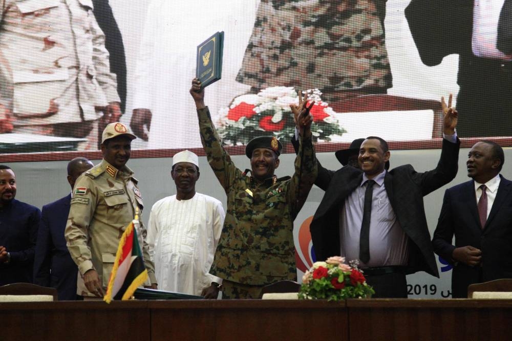 Sudan's protest leader Ahmad Rabie (2nd-right) flashes the victory sign alongside Gen. Abdel Fattah Al-Burhan (center), the chief of Sudan's ruling Transitional Military Council (TMC), during a ceremony where they signed a 