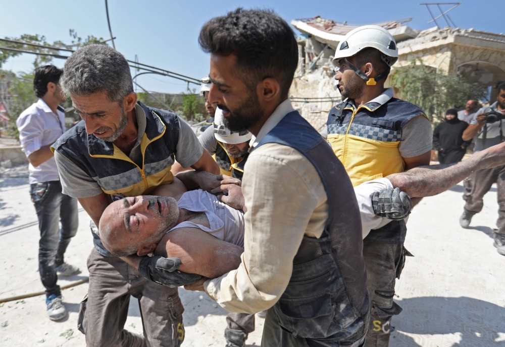Members of the Syrian Civil Defense (White Helmets) carry an injured man after removing him from under the rubble of a building that collapsed during reported airstrikes by pro-regime forces in the village of Beinin, north of Maaret Al-Numan, in the northern Idlib province, Monday. — AFP