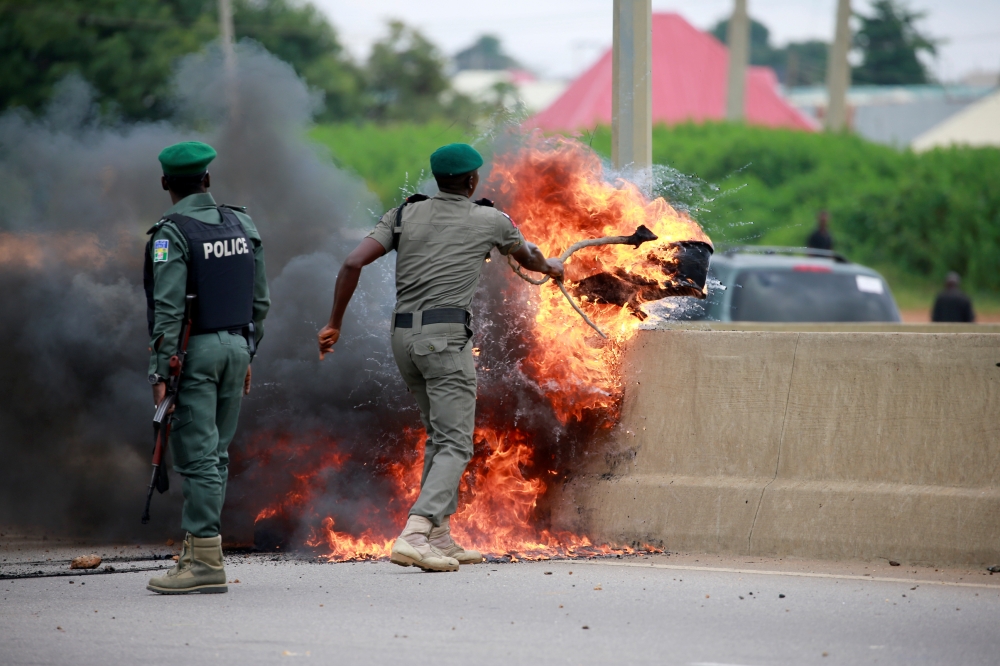 A police office removes burning tires from the road, as protesters set up fires to block traffic along Airport Road in Abuja, Nigeria, on Wednesday. — Reuters