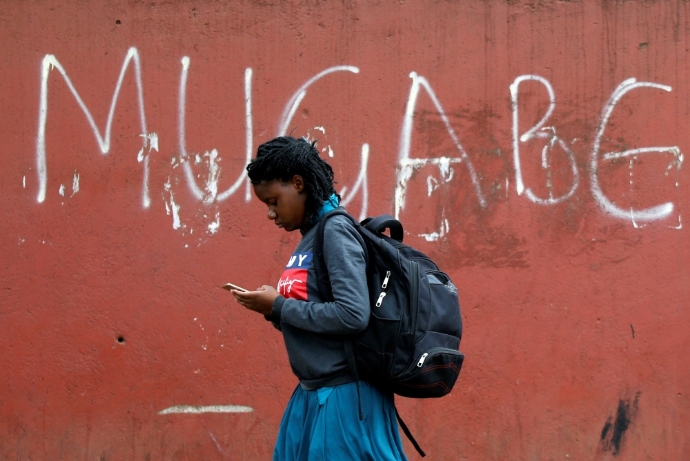 A woman walks past a wall where it's written 