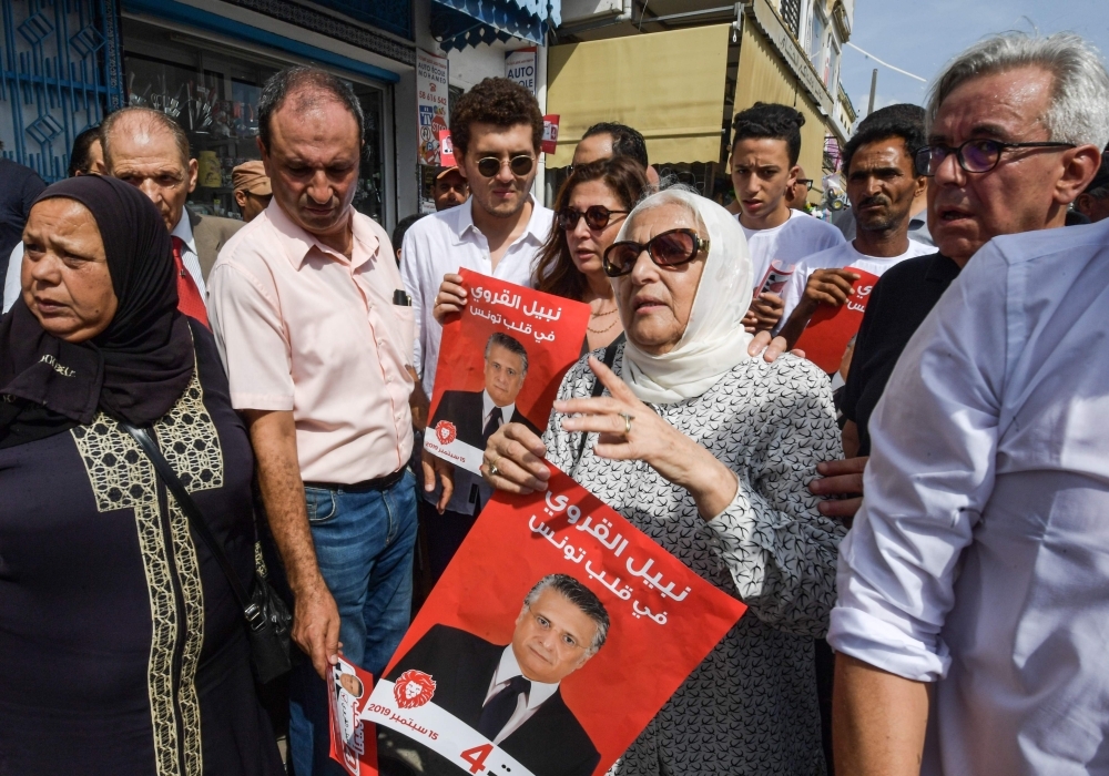 Najiba Karoui, center, mother of Tunisia's jailed presidential candidate Nabil Karoui who faces corruption charges, stands before his sister Rim, center behind, and other supporters with his election poster while campaigning for him in the northern city of Bizerte on Thursday. — AFP