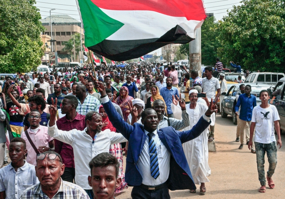 A man flashes the victory gesture while waving a Sudanese national flag during a mass demonstration near the presidential palace in the capital Khartoum on Thursday, calling for the appointment of a new permanent chief of judiciary and prosecutor general. — AFP