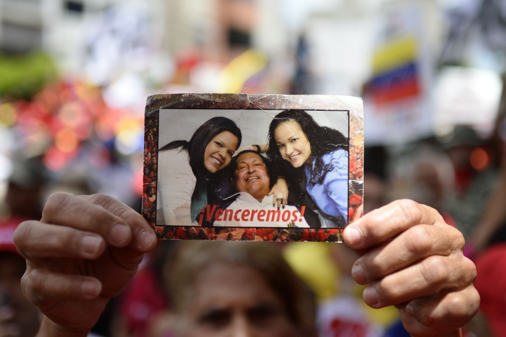 A supporter of Venezuelan President Nicolas Maduro displays a picture of late President Hugo Chavez and his daughters as a lorry carrying boxes with signatures gathered by the government among Venezuelans as part of its 