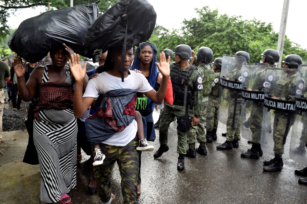 Migrants raise their hands as they walk by members of the National Guard during an operation to halt a caravan of migrants from Africa, the Caribbean and Central America, hours after they embarked toward the United States, in Tuzantan, in Chiapas state, Mexico on Saturday. -Reuters