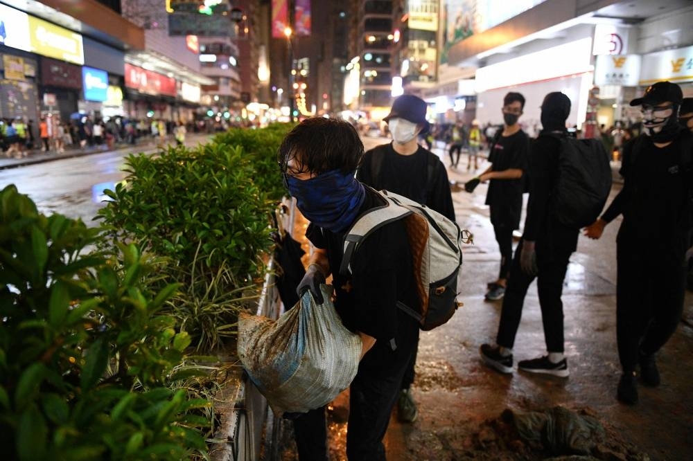 A protester (C) lifts a sandbag as others construct a barricade in the street in the Mongkok area of Kowloon in Hong Kong on Sunday. Hong Kong riot police on October 13 skirmished with small groups of masked pro-democracy protesters who held flashmob gatherings in multiple locations – although crowds were smaller and less violent than recent weekends. — AFP